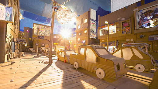 Fotograma de curta-metragem no qual todos os elementos são feitos de papelão e sucata. Por uma rua movimentada passam vários carros em ambos os sentidos. Sobre a calçada há lixos, papéis amassados.